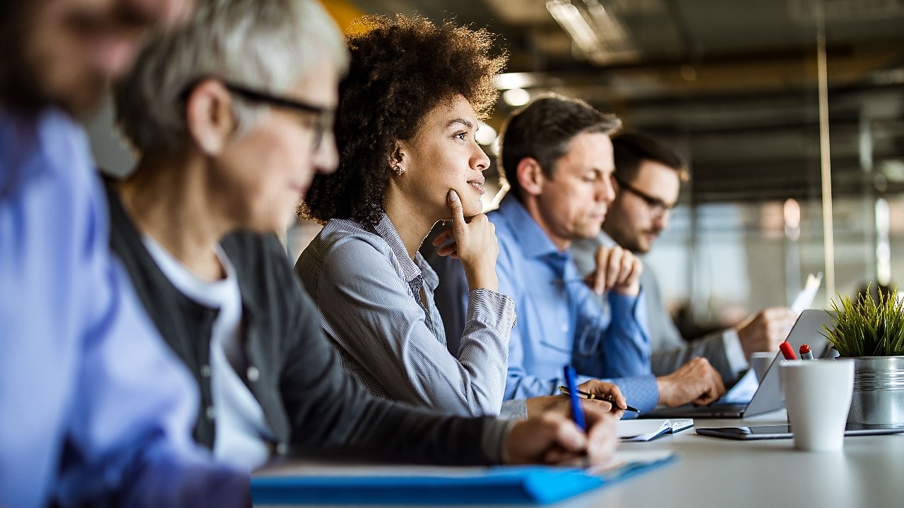 Professionals with laptops and notepads sitting in a row