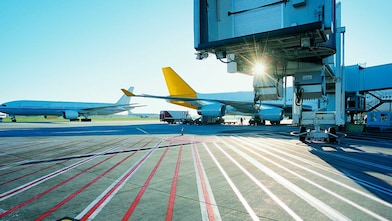View of an airport runway in the early morning with the sun rising over two aeroplanes