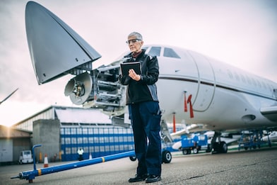 Senior female engineer holding digital tablet next to a a small private airplane with an opened nose cone
