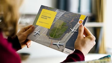A person holding a Shell-branded aviation brochure titled "Cleared for Takeoff”.