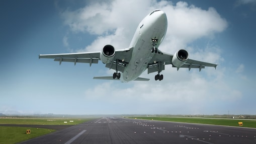 A large commercial airplane taking off from a runway, with its landing gear still extended, against a partly cloudy blue sky.
