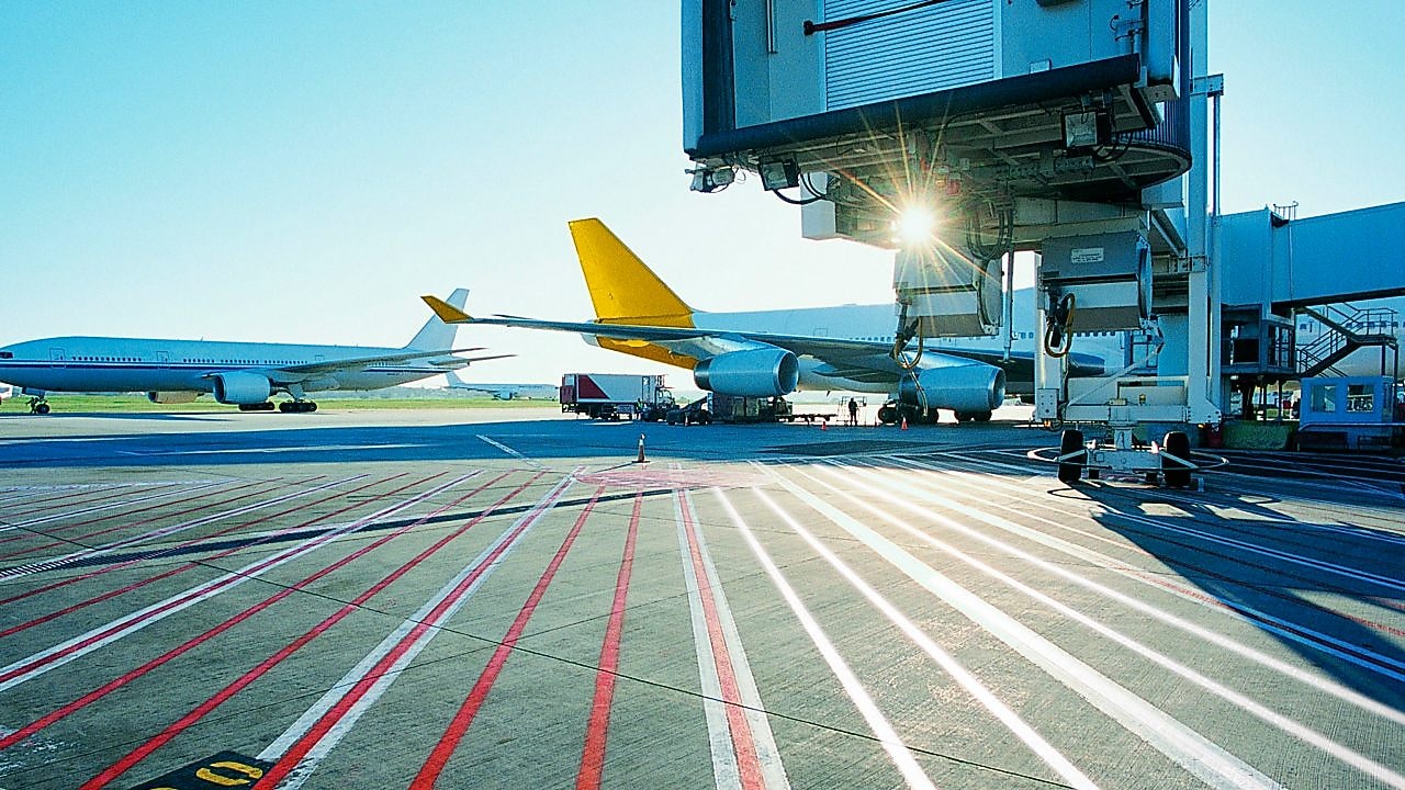 View of an airport runway in the early morning with the sun rising over two aeroplanes