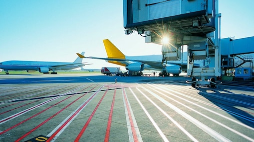 View of an airport runway in the early morning with the sun rising over two aeroplanes