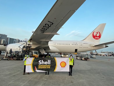 Airport staff holding a "Shell Sustainable Aviation Fuel" banner against the backdrop of a Japan Airlines plane fuelled by SAF
