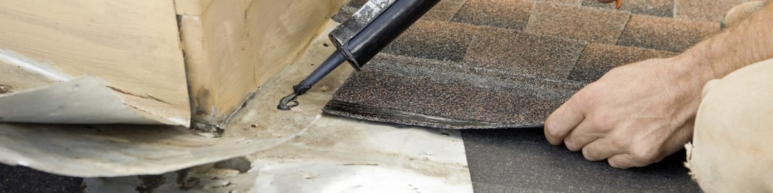 Roofer Applying Caulk to House Chimney Flashing