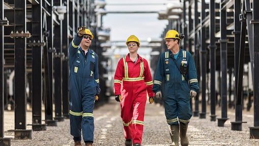 Three workers walk amongst equipment at the Montney Gas Plant