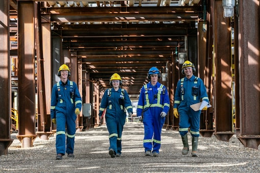 Four people in dark blue jump suits walk toward the camera in front of the Groundbirch project.