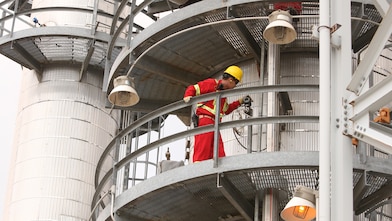 Worker stands on circular platform, examining refinery 