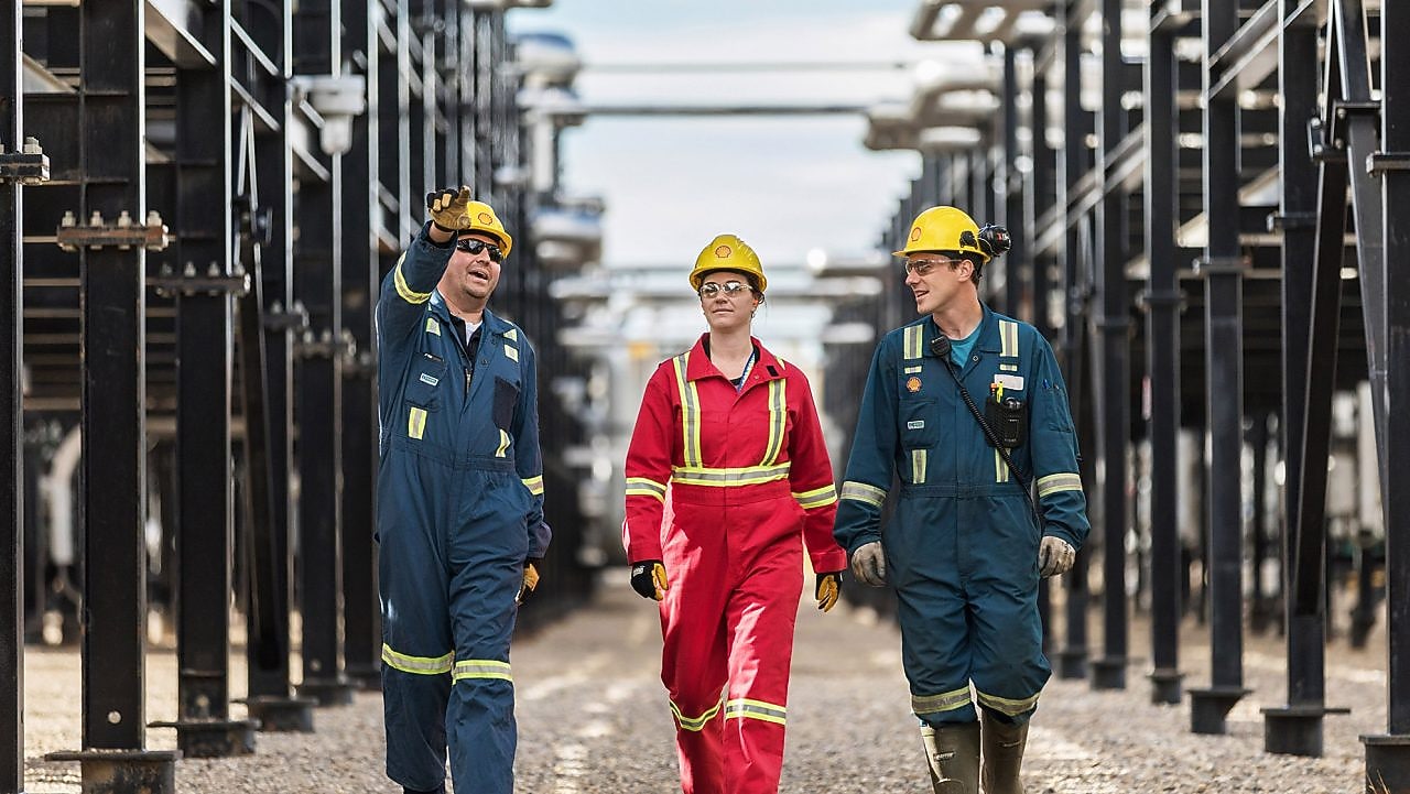 Three workers walk amongst equipment at the Montney Gas Plant