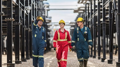 Three workers walk amongst equipment at the Montney Gas Plant