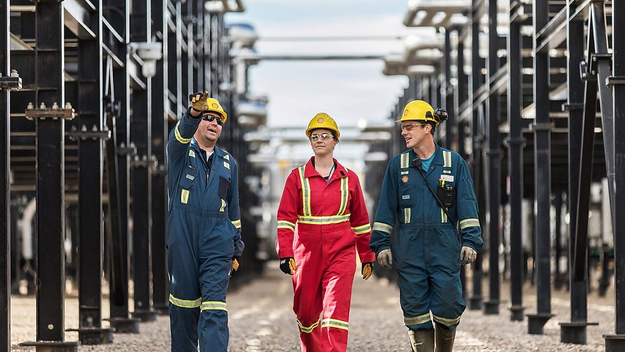 Three workers walk amongst equipment at the Montney Gas Plant