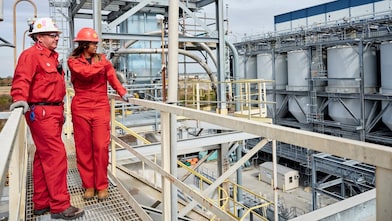 Two workers wearing hard hats discussing inside refinery