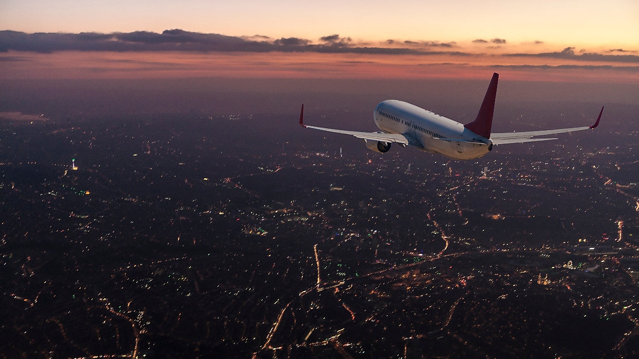Commercial airplane flying over big city at dusk
