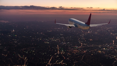 Commercial airplane flying over big city at dusk