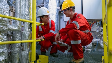 Two workers wearing hard hats discussing inside refinery