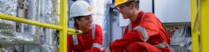 two workers wearing hard hats discussing inside refinery