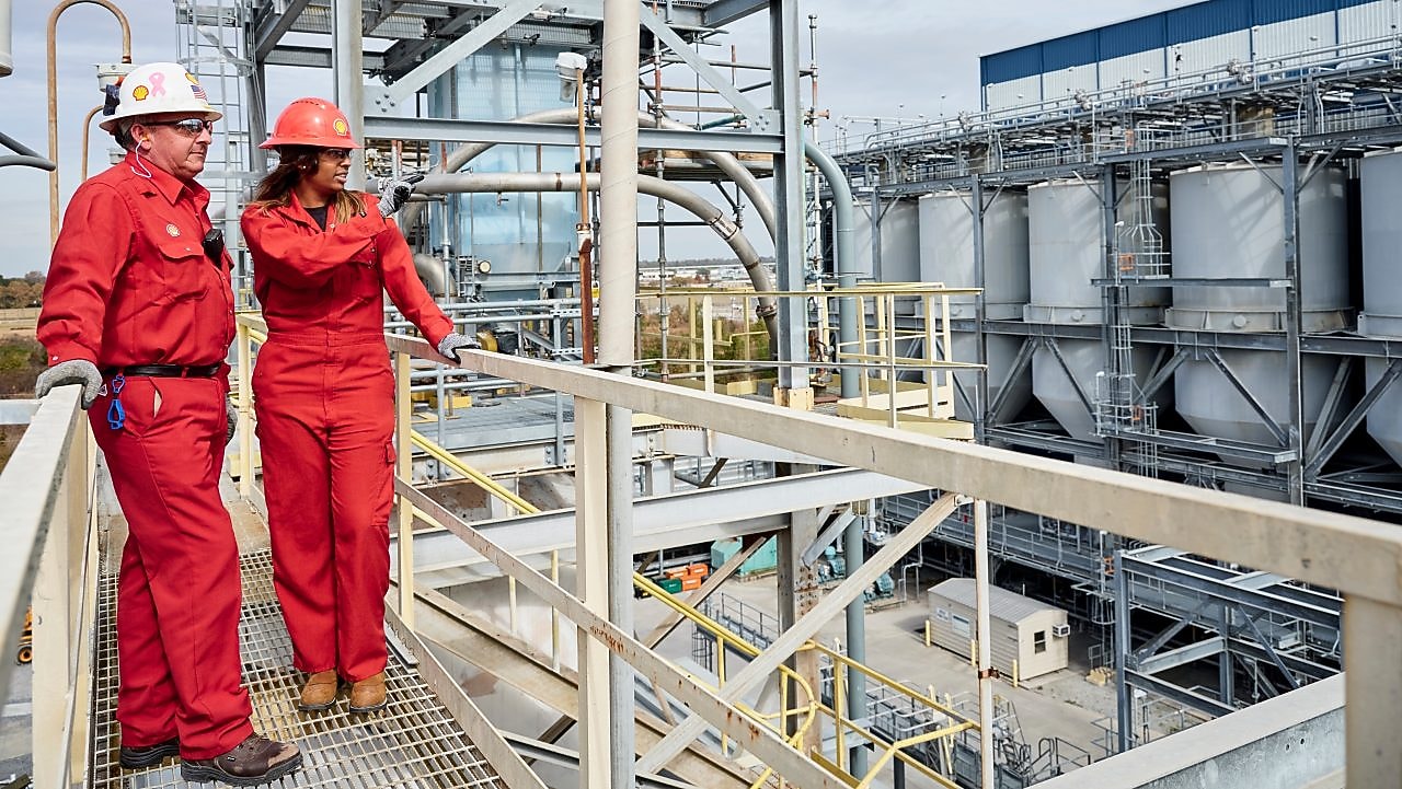 Two workers wearing hard hats discussing inside refinery