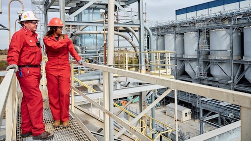 Two workers wearing hard hats discussing inside refinery