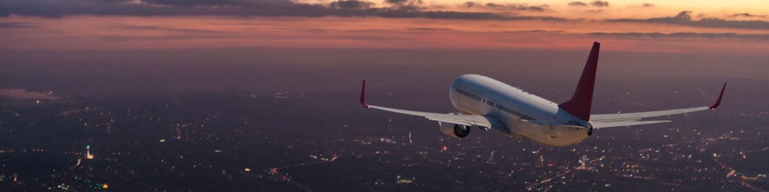 Commercial airplane flying over big city at dusk