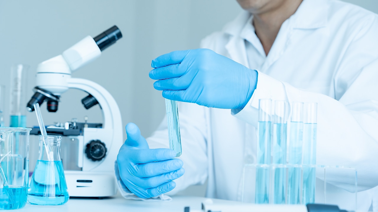 Scientist handling lab glassware next to a microscope