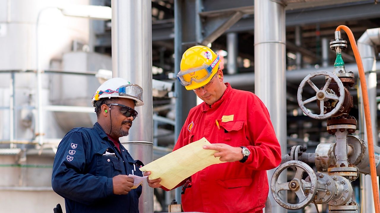 Two workman at a Shell chemical plant discuss plans