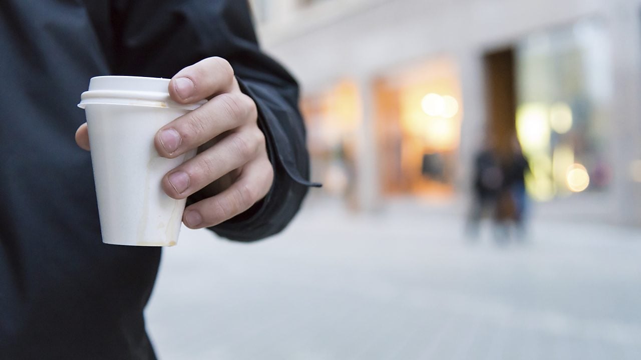 Man holding a styrene cup of hot drink walking on a street