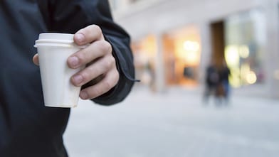 Man holding a styrene cup of hot drink walking on a street
