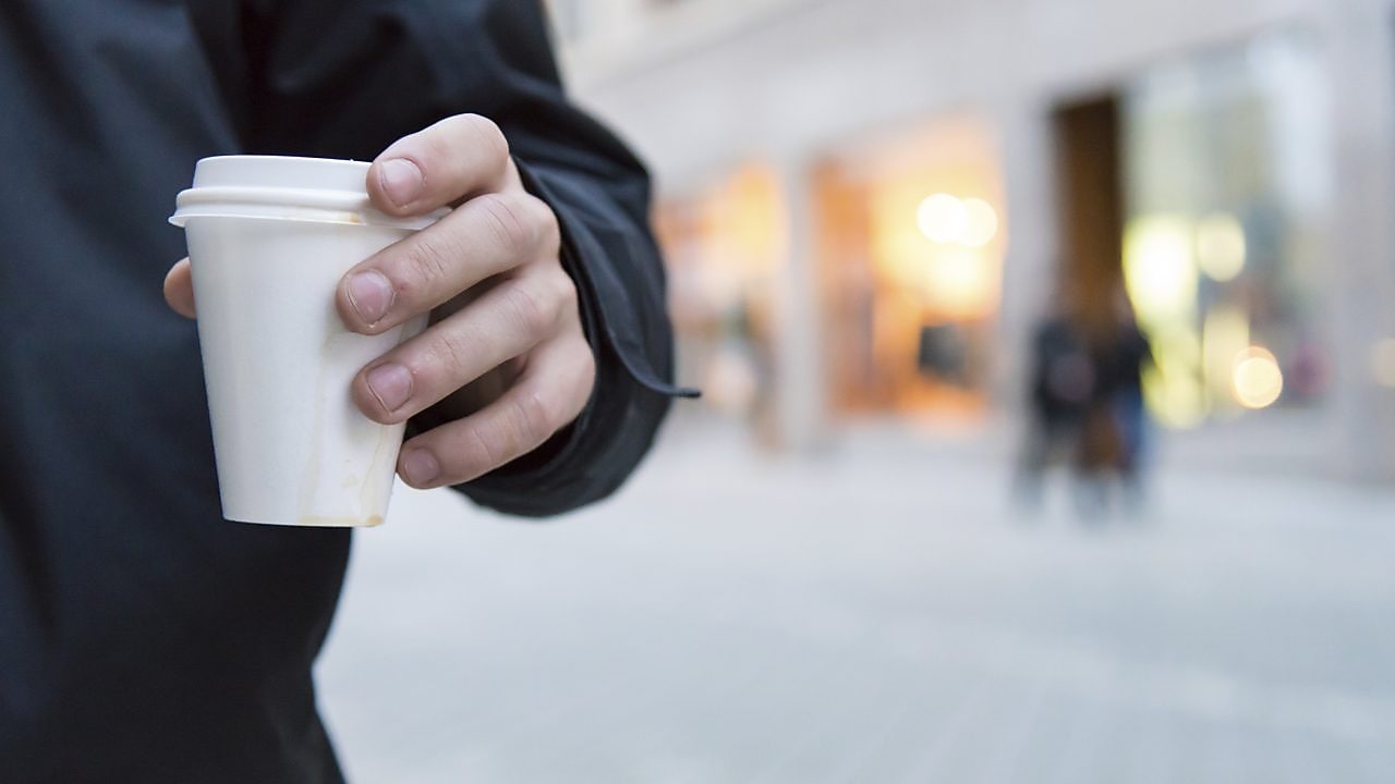 Man holding a styrene cup of hot drink walking on a street