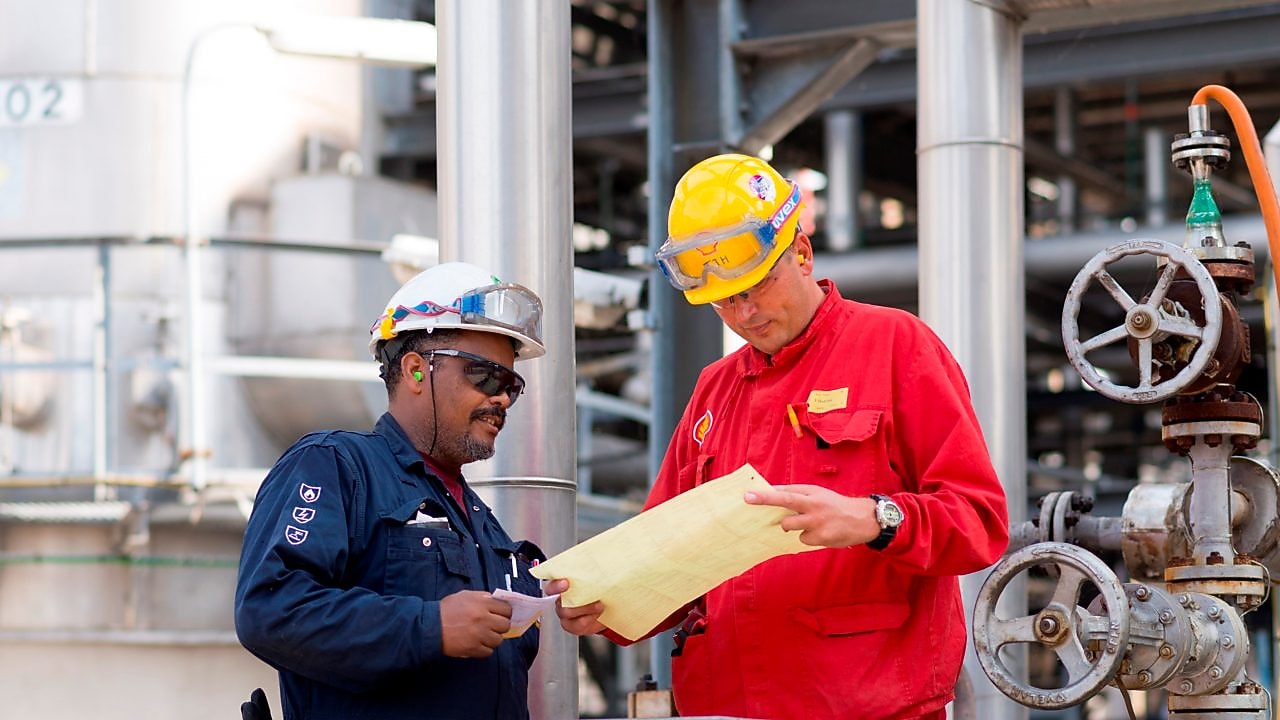 Two workman at a Shell chemical plant discuss plans