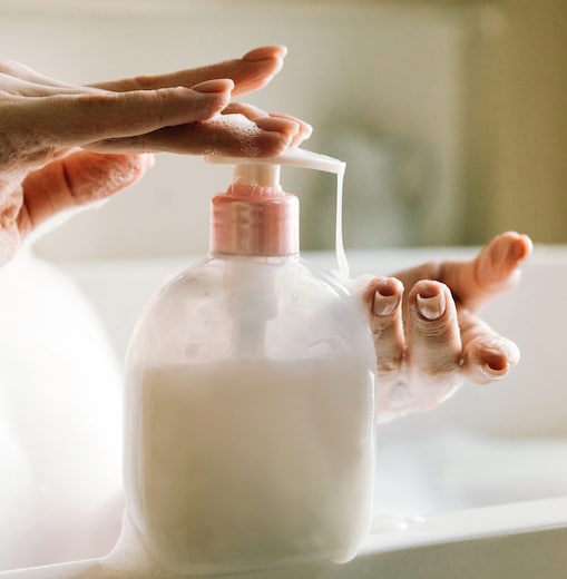 Close-up of hands pressing a foaming soap dispenser in a bathroom sink.