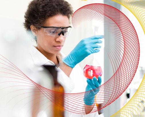 Scientist wearing safety glasses and gloves examining a flask containing pink liquid in a laboratory.