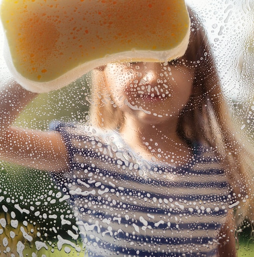 Child cleaning a glass window with a sponge.