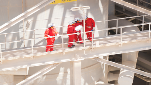 Industrial workers in safety gear reviewing documents on an elevated walkway