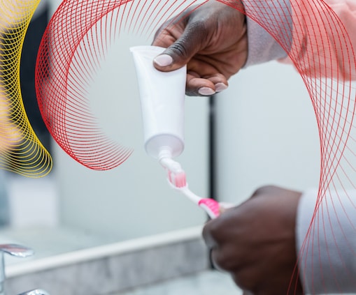 Person putting toothpaste on pink and white toothbrush