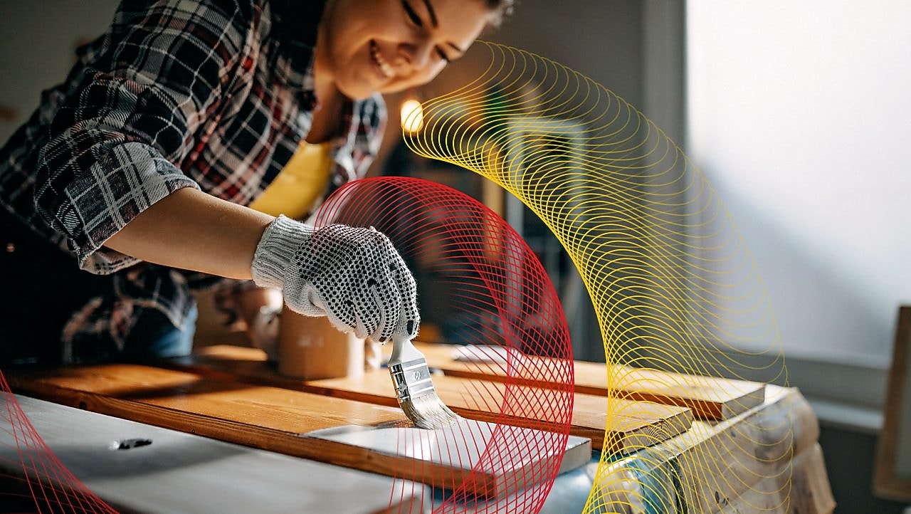 A woman applying white paint to wood boards using a small brush