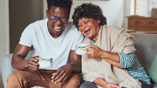 Man and woman on couch laughing with coffee mugs