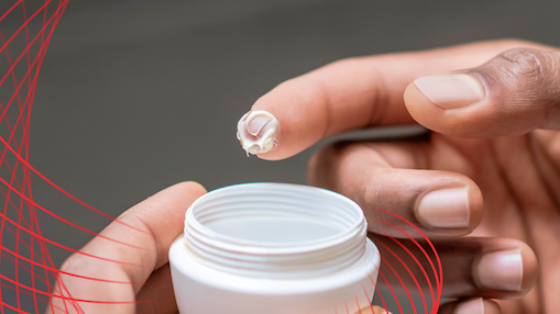 Hand holding a small amount of cream above an open container