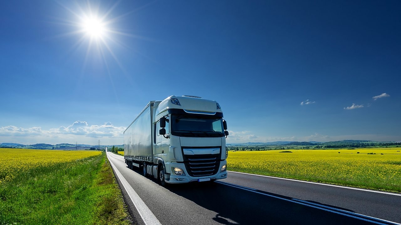 Truck driving on a road past a field