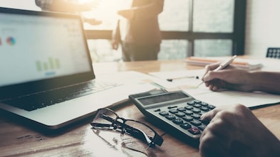 Business team using a calculator and laptop computer to calculate the numbers on his desk in a office