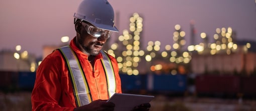 Man holding a tablet device in front of a oil refinery