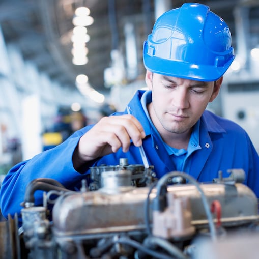 Worker in blue overalls and a helmet working on an engine