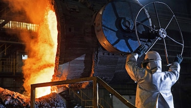 Two factory workers talking next to large rolls of steel