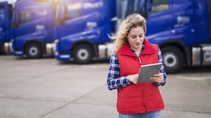 Truck driver holding tablet and checking route for new destination. In background parked truck vehicles. Transportation service.