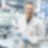 a person in a white coat and goggles holding a bottle of Shell GTL fuel