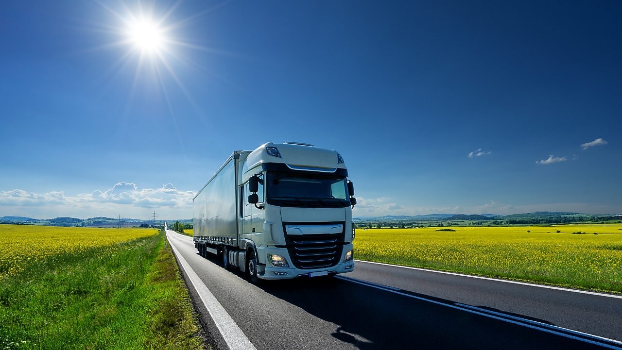Truck driving on a road past a field
