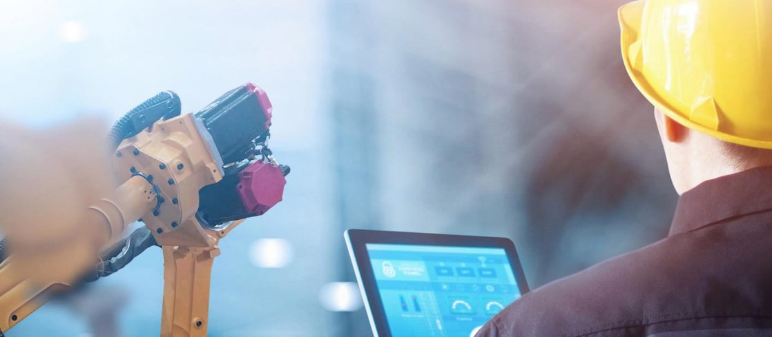 Image of a man with a yellow helmet holding a tablet. He is positioned so his head is turned away from the camera.