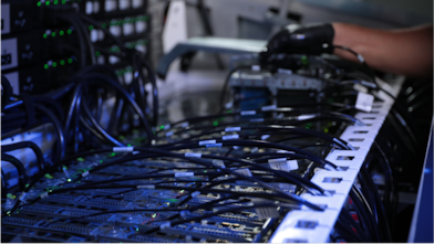 A gloved hand next to an assortment of wires connecting to a computer system.