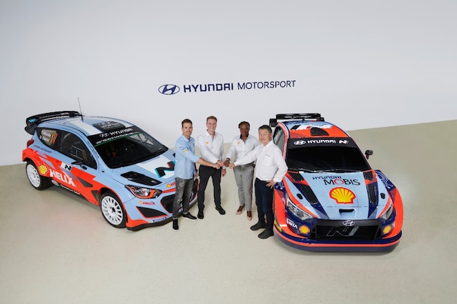 Three men and a women standing beside two cars