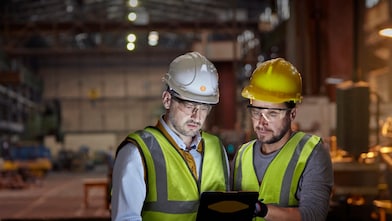 Male engineer and worker using digital tablet in dark factory