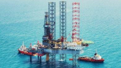 Offshore oil rig platform in open sea, featuring a drilling tower and other equipment, surrounded by  multiple support vessels.